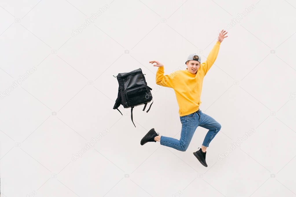 Happy young man jumping with a backpack on a white background. Stylish street boy livid with a backpack on the background of a white wall. Copyspace