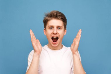 bir sarı arka planda izole beyaz bir T-shirt giyen, ağzına açık kamera görünüyor ile sürpriz bir çocuk portre kaybetmek. Yüzüne yakın elleriyle şok adam kamera bakıyor.