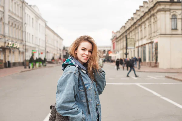 Retrato de uma menina feliz na rua vestindo roupas casuais, jaqueta de jeans, olhando para a câmera e sorrindo. Loira sorridente posa nas ruas da cidade . — Fotografia de Stock