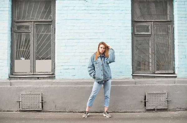 Portrait of a stylish girl at full height against a background of blue wall in retro windows. The girl poses against the background of the old colored wall, looking into the camera. — Stock Photo, Image