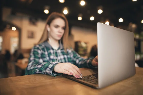 Háttér. Nő ül egy kávézóban egy laptop, hallgat zenét a fejhallgató és működik. Hölgy egy laptop egy hangulatos kávézóban. Fókuszban a laptop és a lány kezét. Elvont homályos fénykép — Stock Fotó