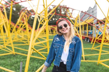 Lunaparktaki, parlak slayt arka planı pozlar şık bir mutlu kız güneş gözlüğü portresi görünüyor kamera ve gülümsüyor. Eğlence Parkı, slaytlar içinde belgili tanımlık geçmiş