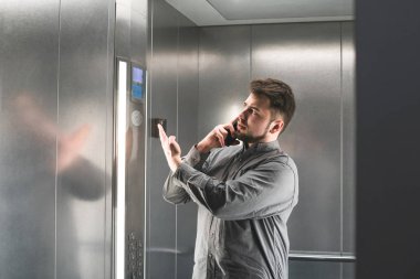 Neşeli işadamı asansörde telefon tarafından bir şey açıklayan, gömlek giyiyor. Genç adam çalışan onun akıllı telefon ve aktif jestleri üzerinde konuşma ifade ediyor