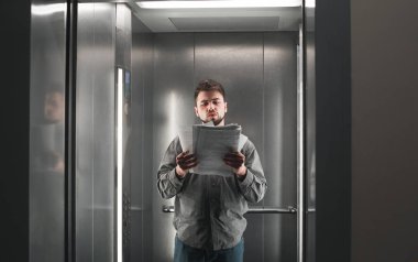 Genç bir erkek çalışanın portresi asansörde duran belgeleri okuyor. Konsantre işadamı asansördeki dokümanları kontrol ediyor.