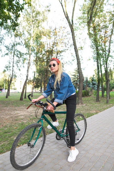 スタイリッシュな魅力的な女性は自転車に乗って公園に立っているし、スマート フォンを使用します。スマート フォン上女の子の自転車ルートを見る. — ストック写真