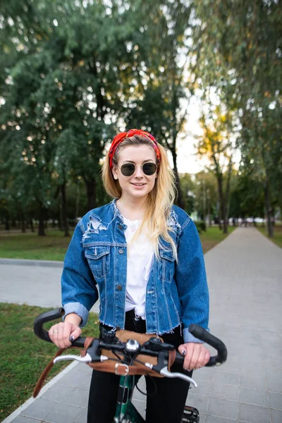 スタイリッシュな魅力的な女性は自転車に乗って公園に立っているし、スマート フォンを使用します。スマート フォン上女の子の自転車ルートを見る. — ストック写真