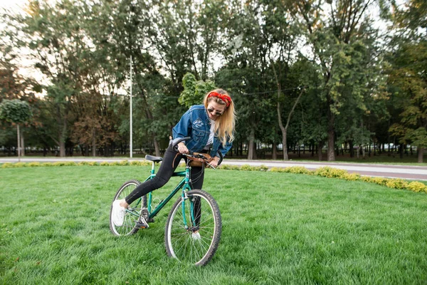 公園で自転車で完全な高さに肯定的な女性の肖像画。女の子はバイクで芝生の上に立って、移動を開始します。公園で自転車の上を歩きます。アクティブなレジャーの概念. — ストック写真