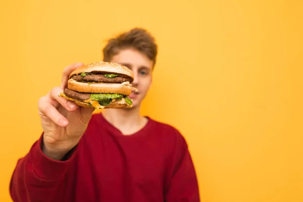 Tle. Zbliżenie Burger w rękach młodego mężczyzny. Facet trzyma w dłoniach szybkie szkodliwe jedzenie. Kanapka jest w rękach głodnego faceta. — Zdjęcie stockowe