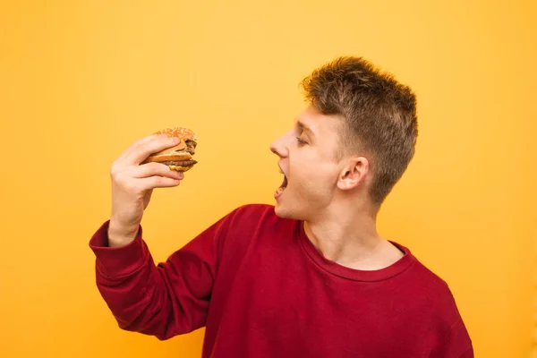 Счастливый парень с аппетитным бургером в руках изолирован на — стоковое фото