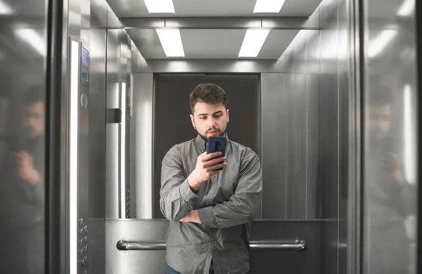 Busy man employee is watching on her smartphone screen in the lift. Shot of the businessman in the elevator using her smartphone. — Stock Photo, Image