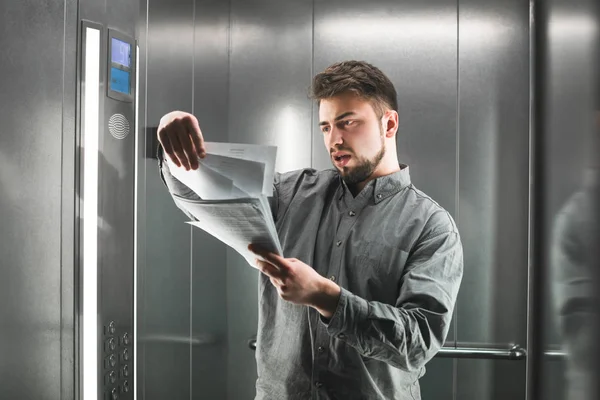 Hombre de negocios concentrado con camisa leyendo los documentos en el ascensor. El trabajador de oficina sorprendido está mirando papeles y examinando en el ascensor. Hombre de negocios sorprendido — Foto de Stock