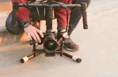 Bir Kameracı bir adamın yakın çekim fotoğraf, elinde bir stabilizatör ve gün batımı arka planda Evil kamera tutar. Sokakta video çekim süreci. Boşaltmak