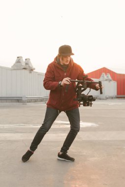 Elinde DSLR kamera için bir sabitleyici ile bir adamın portresi yürür ve video alır. Kameracı bir sabitleyici ile bir video alır. Adam sokakta stabilizatör videosunu çeker. Backstage