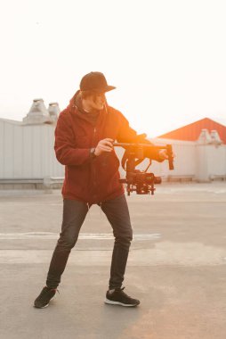 Gün batımı arka planda sabitleyici ve kamera ile Videographer. Bir adam portresi elinde bir kamera ile bir stabilizatör tutar ve video alır. Creator bir video oluşturur