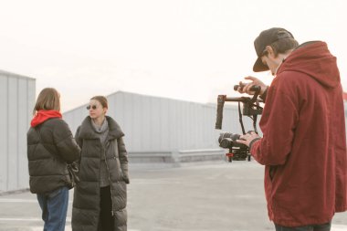 Videograför DSLR kamera ile bir stabilizatör elinde tutan ve sokakta iki kız video alır. Video klipleri oluşturma işlemi. Profesyonel kameraman video blogcular kaldırır