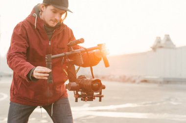 Elinde bir stabilizatör ile kameraman üzerinde bir video vuruyor DSLR gün batımı arka planda kamera. Backstage konsepti