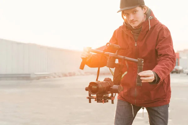 Videographer with gimball video dslr.Portrait of the cameraman with a stabilizer in his hands shoots a video on the dslr camera on the background of the sunset. Man with a stabilizer creates a video — Stock Photo, Image