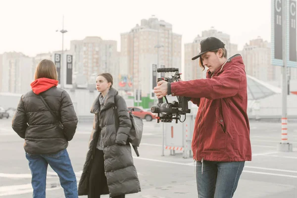 Videographer shoots video of two stylish girls, posing on the camera. Backstage. Cameraman holds in the hands of a stabilizer with dslr camera and takes video of two girls on the street