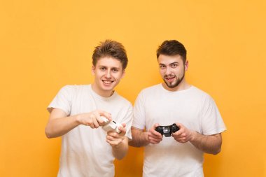 Ellerinde joystick ile arkadaşlar sarı bir arka planda, kamera bakarak ve video oyunları oynuyor. İki kişi konsolda video oyunları oynar. Konsol kavramı oyunu.