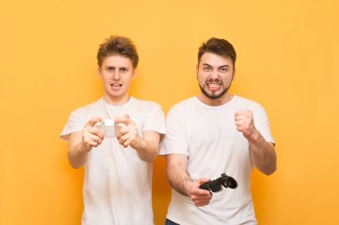 Beyaz T-shirt iki oyuncu elleriyle joystick tutmak ve sarı bir arka planda izole, duygusal video oyunları oynamak. İki duygusal adam kendi ellerinde joystick ile oyun oynamak.
