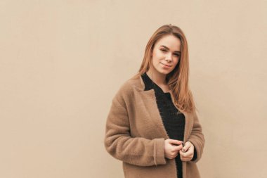 Bahar giysileri güzel Bayan, kahverengi bir ceket giyiyor, bir bej duvarın arka planda ayakta, kamera bakarak. Duvar arka plana karşı şık kız. Boşaltmak