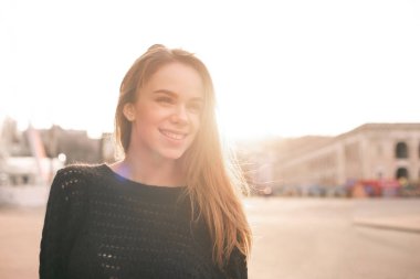 Rahat giyim mutlu kız, gün batımı sokak manzara arka planda ayakta, yan bakıyor ve gülümseyen. Sokakta güzel bir Bayan portre gülümseyen ve kamera poz