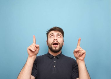 Mavi bir arka planda sürpriz bir adamın portresi, görünümlü ve boş bir alan üzerinde parmaklarını gösteren. Sakal olan adam copyspace üzerinde eller gösterir, izole