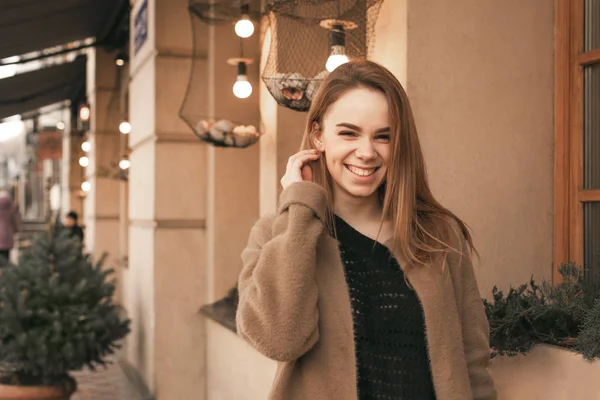 Porträt eines glücklichen Mädchens, das durch die Stadt läuft, an der braunen Wand steht, frühlingshafte Kleidung trägt, in die Kamera schaut und lächelt. — Stockfoto