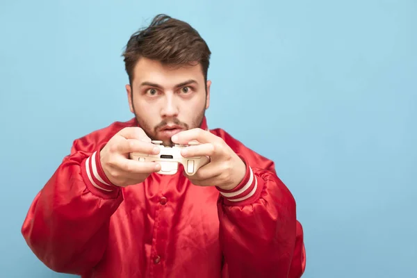 Retrato de um jogador adulto emocional com um joystick na mão sobre um fundo azul, concentrado na câmera. Concentre-se no gamepad . — Fotografia de Stock