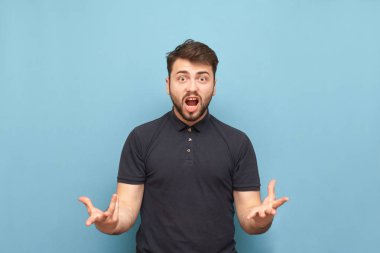 Karanlık bir tişört içinde Expresive sakallı adam mavi bir arka planda sevindiler. duygusal sevinçler, eller kaldırdı, mavi bir arka planda izole. Adamın takımının zaferine sevinme. Boşaltmak