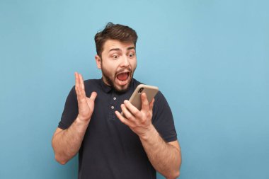 Elinde bir akıllı telefon ile çılgın sakallı bir adamın portresi, ekrana bakarak ve mavi bir arka planda çığlık. Şok adam bir akıllı telefon ve sevinler kullanır. Izole.