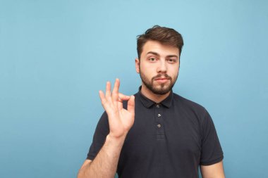 Mavi bir arka planda sakal ayakta koyu bir gömlek giyen güzel bir esmer adam portre, elini ile ok bir jest gösteren, ciddi bir yüz ile kamera bakarak. Izole