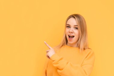 Sarı bir arka plan üzerinde izole, yan başparmak gösteren sürpriz tatlı bayan Portresi. Duygusal kız şok edici bir yüz ile uzağa bakar ve reklam için bir yerde parmağını gösterir. Kopyalama alanı