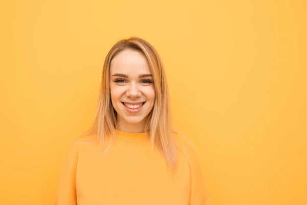 Retrato de close-up de uma adolescente sorridente em um fundo laranja, vestindo uma roupa casual, olhando para a câmera e se alegrando. Menina positiva isolado no fundo amarelo . — Fotografia de Stock