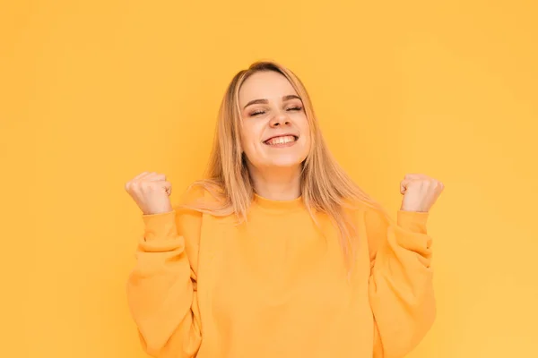 Vrolijke meid in heldere kleren blij met haar handen op een gele achtergrond. Portret van een meisje verheugt in de overwinning met een gelukkig gezicht, geïsoleerd op een gele achtergrond. Ruimte kopiëren — Stockfoto