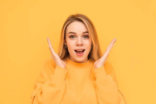 Το κοντινό πορτρέτο ενός ελκυστικού νεαρού κοριτσιού με ένα σοκαριστικό πρόσωπο κοιτάζει την κάμερα. Η έκπληκτη ξανθιά με πορτοκαλί ρούχα απομονώνεται σε κίτρινο φόντο. Αντιγραφή χώρου — Φωτογραφία Αρχείου