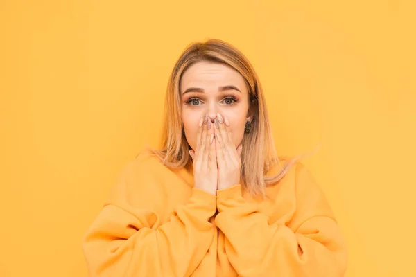 Retrato de close-up de uma garota chocante em roupas brilhantes, suas mãos fecharam a boca e olharam assustadas para a câmera em um fundo amarelo. Isolados . — Fotografia de Stock