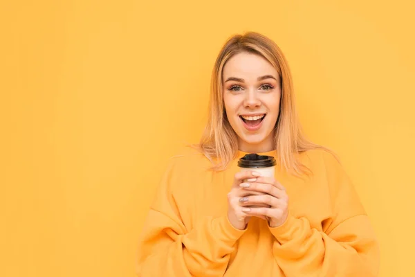 Gros plan portrait d'une fille expressive avec une tasse de café dans les mains, regarde la caméra avec un visage surpris sur un fond jaune. Isolé . — Photo