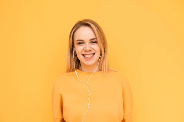 Vriendin's close-up portret houdt van muziek op een koptelefoon op een oranje achtergrond, luistert naar muziek, glimlacht en kijkt naar de camera. Lady muziekliefhebber luistert graag naar muziek. Geïsoleerd — Stockfoto