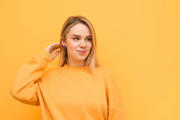 Lieve dame in een oranje trui poses op een gele achtergrond, kijkt opzij in een lege ruimte en glimlacht. Mooi, positief meisje kijkt naar de plaats voor reclame. Geïsoleerd. — Stockfoto