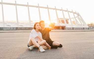 Güzel mutlu çift, bir akıllı telefonun kameraya bakarak ve gülümseyen gün batımı arka planda fotoğraf yapar. Çift güzel bir şehir manzara Lifestyle arka planda bir selfie alır