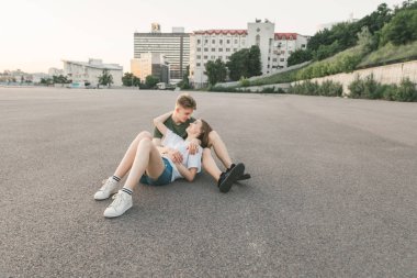 Rahat giysiler şık bir çift fotoğrafları birbirlerine bakıyor ve gülümsüyor, sarılma vardır. Lifestyle.Happy genç adam ve kız sarılmak, şehrin arka planında yere oturan