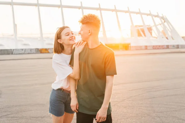 Couple aimant un jeune homme et une fille debout sur le fond du coucher de soleil, se regardant et souriant.Histoire d'amour d'une photo de jeunes gens élégants sur le fond d'un beau paysage — Photo