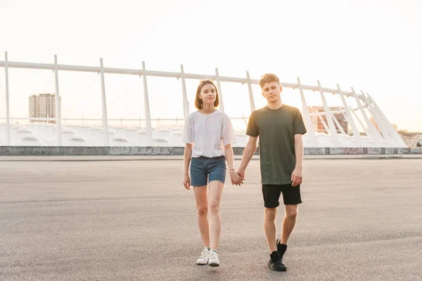 Mooie mooie paar wandelingen door handen te houden in de achtergrond van het stadslandschap, kijkend naar de camera en glimlachend. Portret stijlvolle paar casual kleding in de achtergrond van de stad — Stockfoto