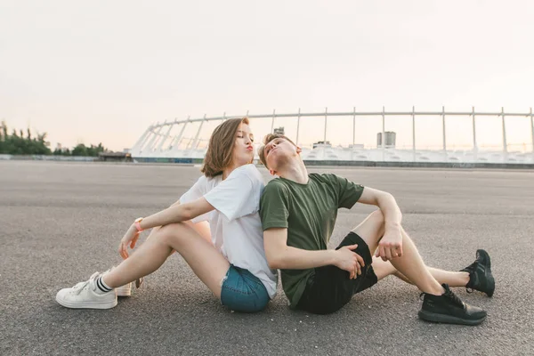 Lieve mooie paar zit 's avonds op het dak en kusjes, het dragen van stijlvolle kleding, de man en het meisje kijken naar elkaar. Leuk paar wil de stedelijke achtergrond kussen. — Stockfoto