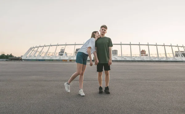 Portret młodej pary zakochany w tle wieczornego krajobrazu miasta. Para stoi na ciepłym letnim wieczorem na dachu trzymając ręce dziewczyna uściski chłopca, młody człowiek patrzy na kamerę. — Zdjęcie stockowe