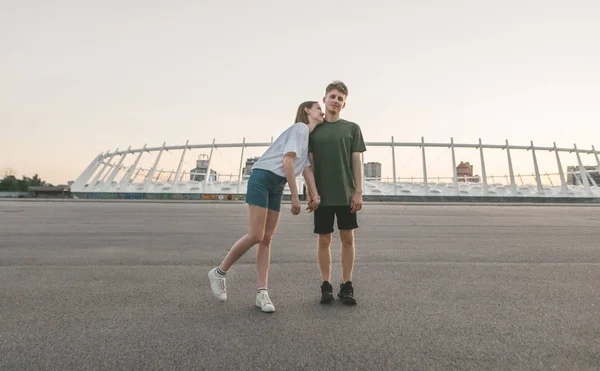 Portrait d'un jeune couple amoureux de l'arrière-plan du paysage urbain du soir.Couple debout sur une chaude soirée d'été sur le toit tenant la main fille étreint le garçon, jeune homme regarde la caméra . — Photo