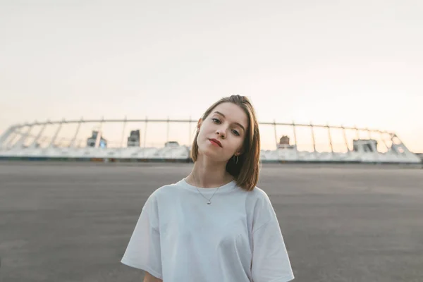 Retrato da noite de uma menina atraente com um rosto sério olhando para a câmera. Uma menina bonita e bem vestida vestindo roupas casuais posa para a câmera . — Fotografia de Stock