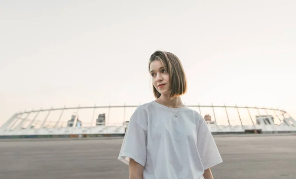 Retrato de menina atraente em t-shirt branca no fundo urbano, olhando para longe. Noite rua retrato de uma menina bonito . — Fotografia de Stock