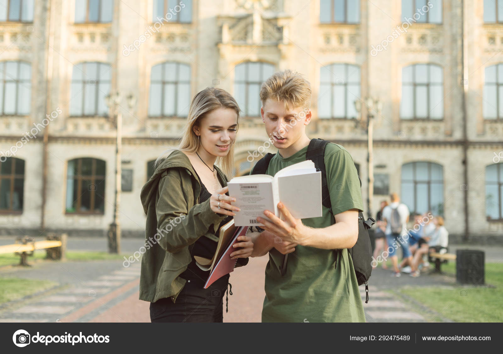 대학 앞에 서있는 젊은 매력적인 귀여운 학생 부부는 흥미로운 책을 읽고. 수업을 준비하는 대학 근처에서 책을 읽는 두 명의 집중된 학생이  놀랐습니다.. — 스톡 사진 © bodnarphoto #292475489, image size:1600x1126